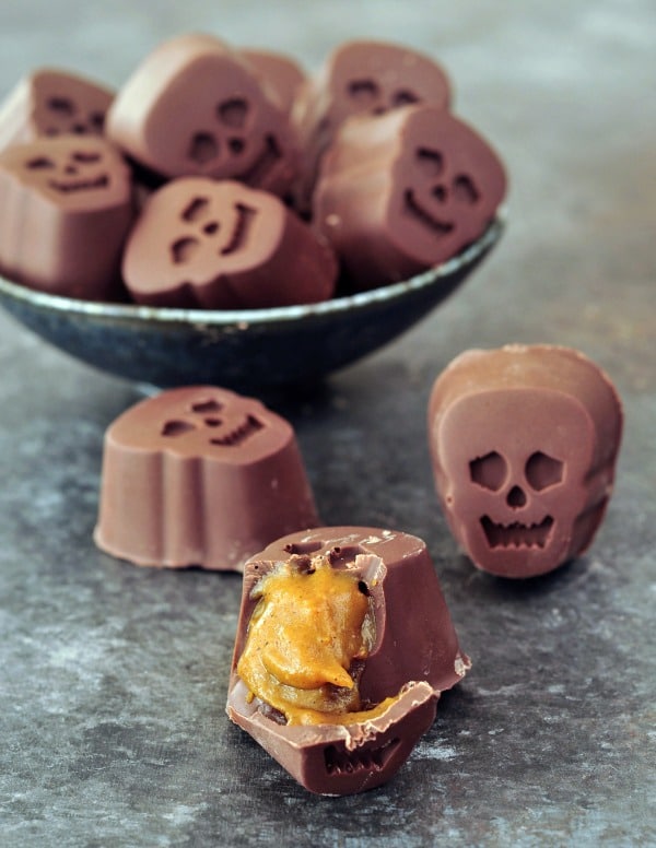 a bowl full of bite size, skull shaped Halloween chocolates stuffed with pumpkin caramel. one outside of the bowl is cut open to show the golden caramel inside.