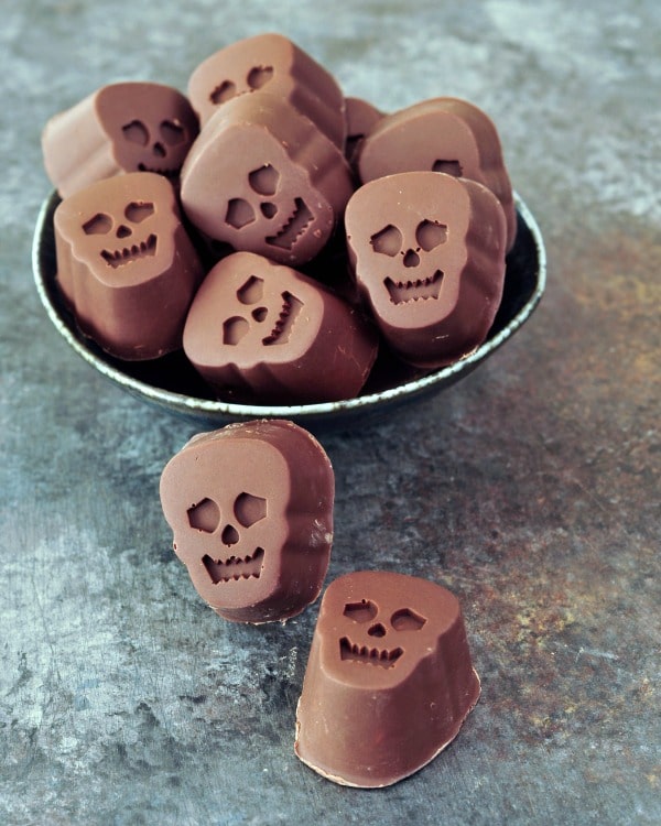 bite size, skull shaped Halloween chocolates stuffed with pumpkin caramel, in a bowl on a dark marbled background