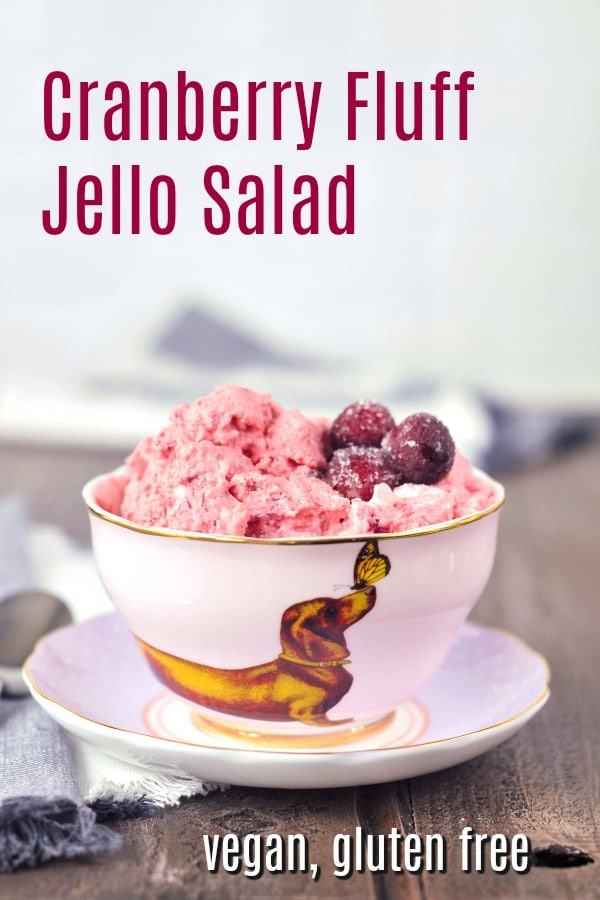 bright pink vegan cranberry fluff jello salad served in a light pink china tea cup and saucer, topped with sugared cranberries