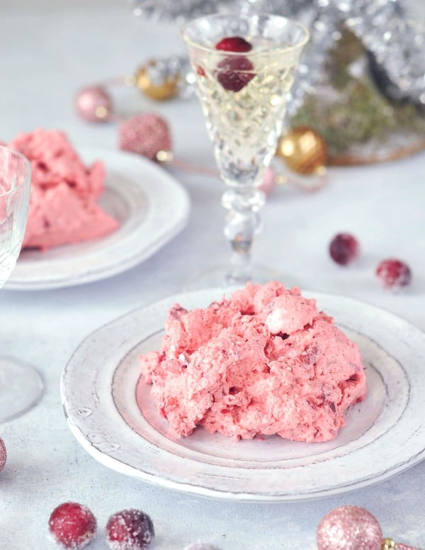 single servings of bright pink cranberry fluff jello salad on rustic white plates, sugared cranberries and champagne glasses in the background