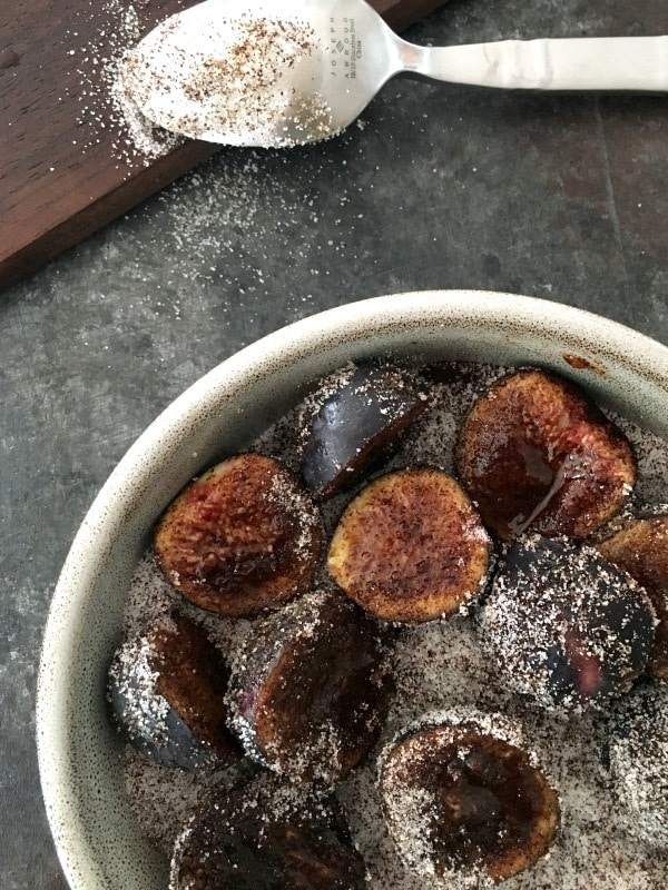 Sliced figs in a shallow bowl after being stirred / coated with espresso powder and sugar. a sugar dusted spoon on the side.