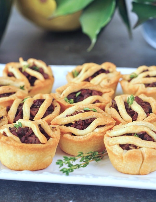 Mini vegan sausage pies on a white square platter dressed with sprigs of fresh thyme.