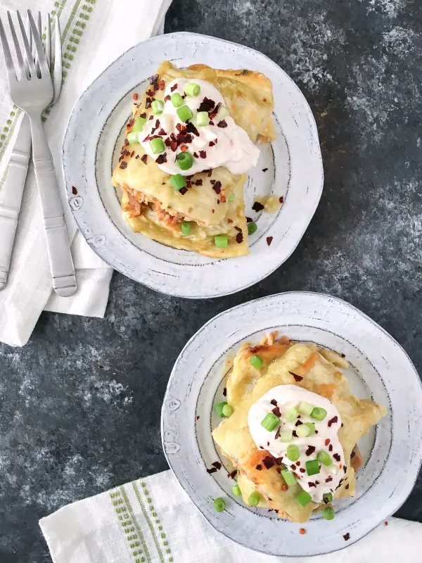 overhead view of Vegan Buffalo Jackfruit Enchiladas sliced in half and stacked on a grey rustic plate, insides filled with orange buffalo sauced, shredded jackfruit, rice, topped with avocado slices and red chile flakes.