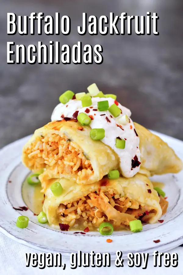 Vegan Buffalo Jackfruit Enchiladas sliced in half and stacked on a grey rustic plate, insides filled with orange buffalo sauced, shredded jackfruit, rice, topped with sour cream and sliced green onion.