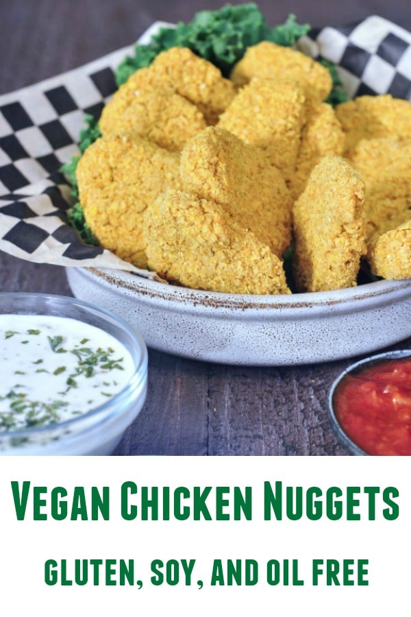 Vegan chicken nuggets in a shallow bowl with black and white checkered paper and kale garnish. dipping sauces on the side (ranch, teriyaki sauce, tomato)