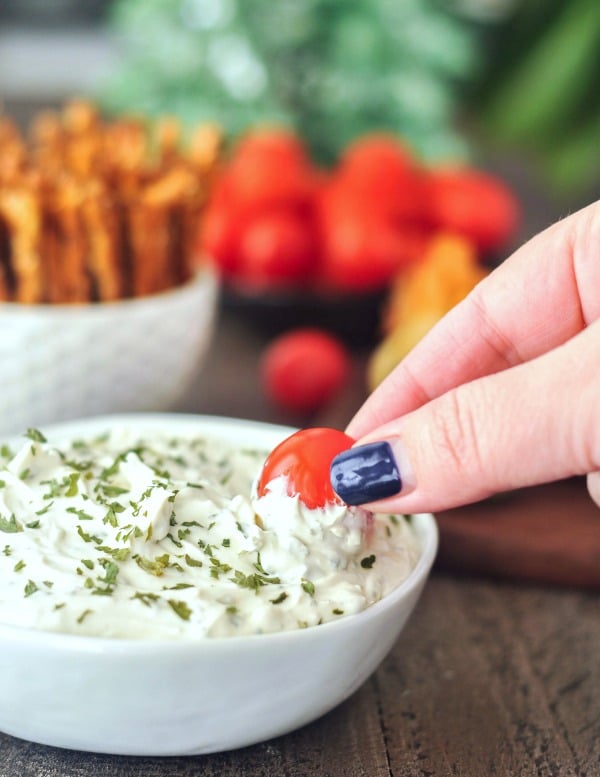 a hand dipping a fresh tomato into a bowl of homemade Boursin style cheese spread