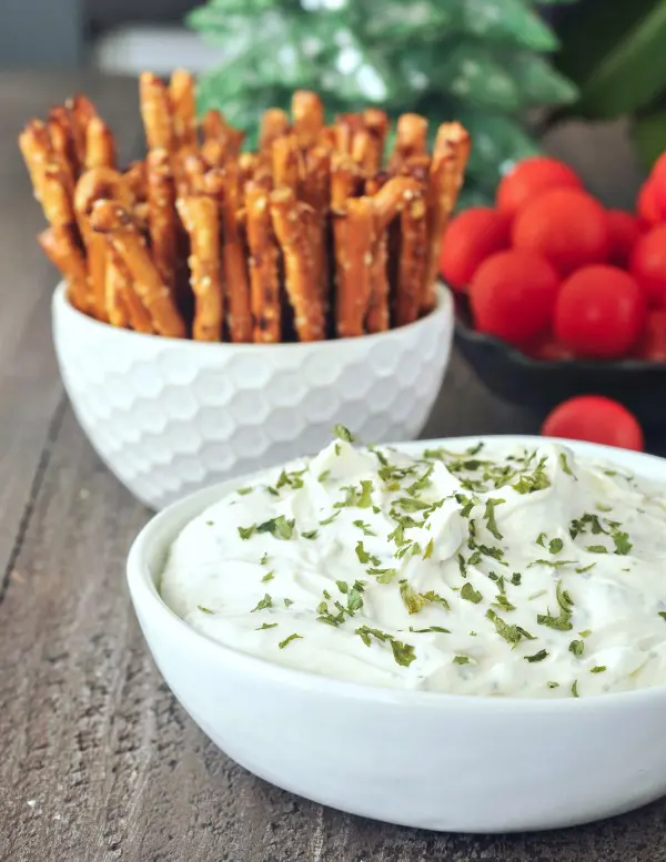 vegan Herb Cheese spread in a white ceramic serving bowl, pretzels and vegetables for dipping