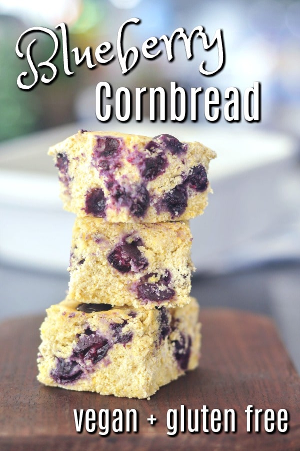 squares of Blueberry Cornbread stacked three high on a dark brown wood cutting board