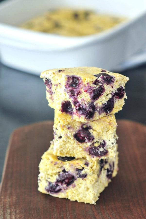 squares of Blueberry Cornbread on a cutting board, baking pan with the remaining cornbread in background