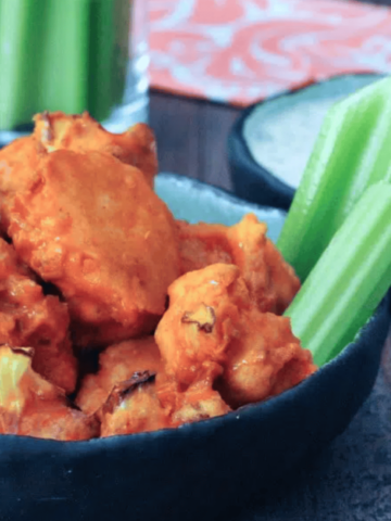 Vegan air fryer buffalo cauliflower served in a bowl with celery and ranch dressing on the side