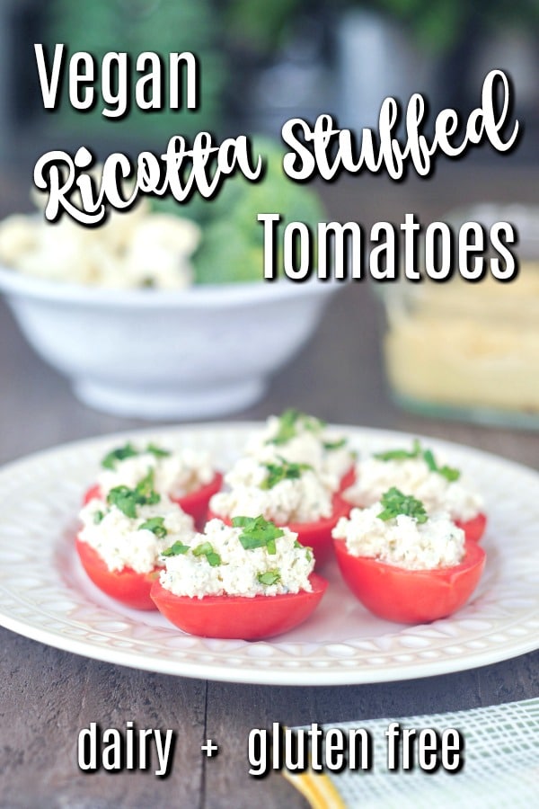 Vegan Ricotta Stuffed Tomatoes topped with fresh chopped basil, sitting on a plate with other appetizer dishes in background