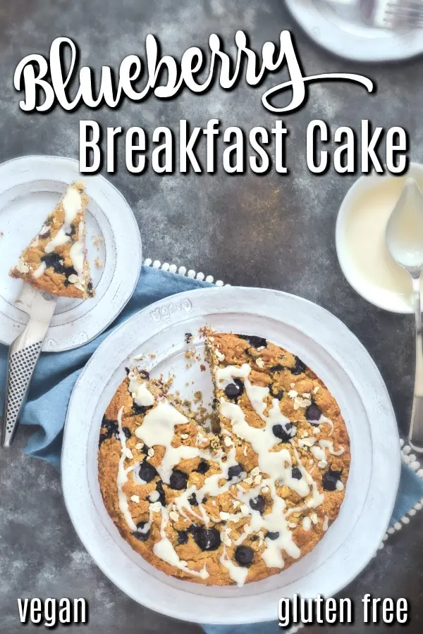 overhead view of Healthy Coffee Cake / Blueberry Breakfast Cake - full cake on platter, one slice on a serving plate, small bowl of icing on the side