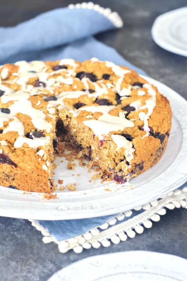 Healthy Coffee Cake with blueberries and glaze, on a white plate with one slice out