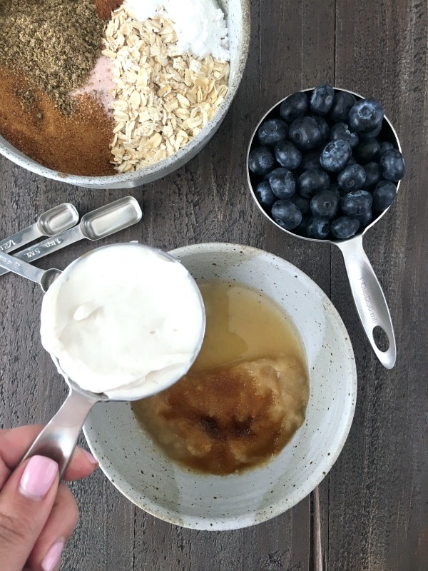 Healthy Coffee Cake step by step: measuring yogurt into bowl of wet ingredients, cup of fresh blueberries and bowl of dry ingredients also in view