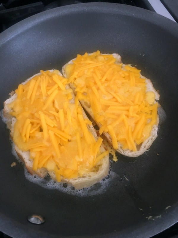 How To Make A Jalapeno Popper Sandwich: slices of bread in a buttered skillet, topped with grated cheese