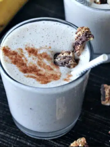 pale tan colored snickerdoodle smoothies in short glasses, garnished with cinnamon and granola, a bunch of banana in background