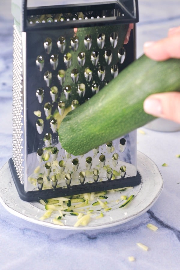 shredding a zucchini with a box grater on a plate