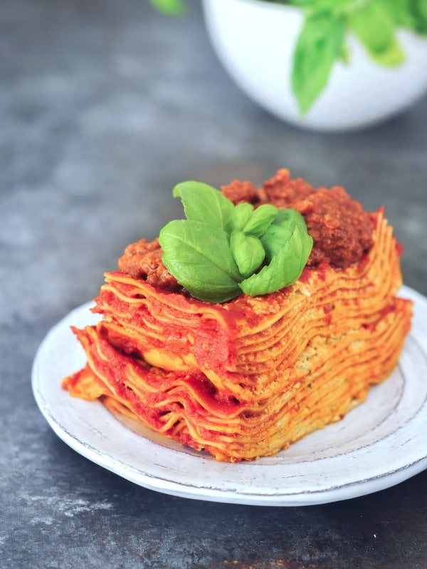 twelve layer slice of gluten free Vegan Lasagna on a rustic plate, garnished with fresh basil