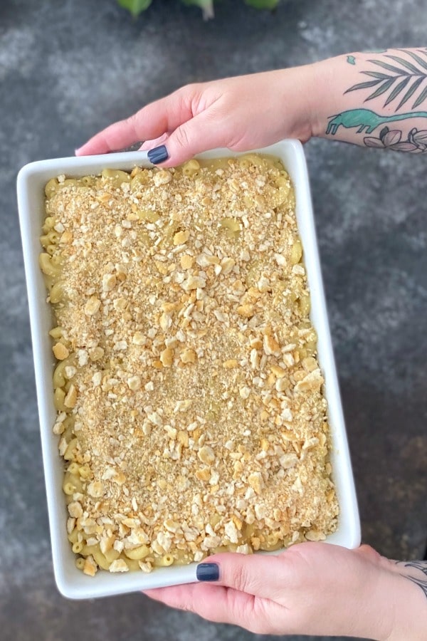 hands holding a full baking dish of vegan baked mac and cheese