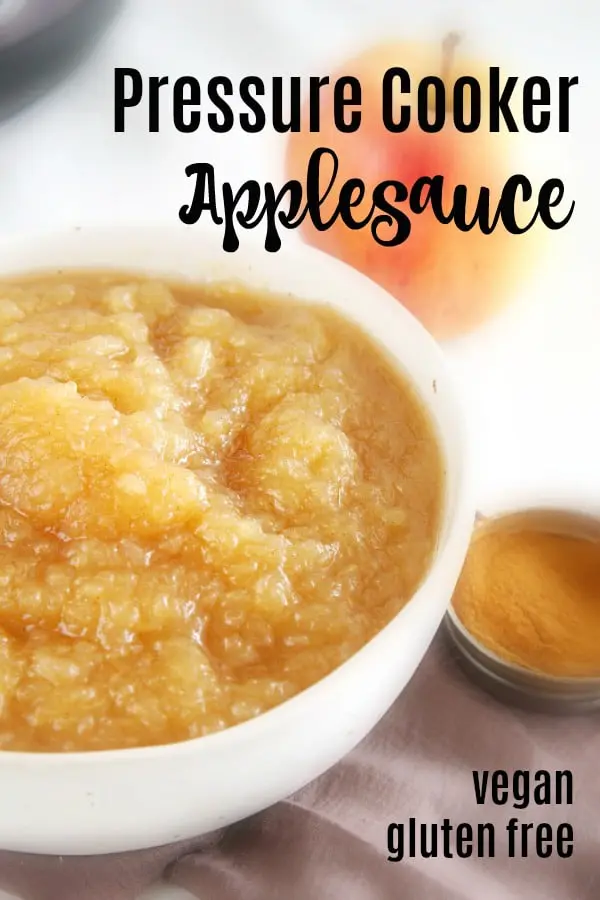 white bowl of applesauce, a whole apple and small container of cinnamon on the side