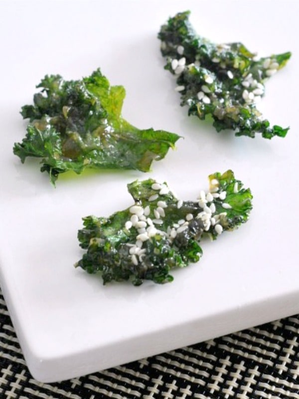 Bright green crispy kale chips with miso and sesame seeds served on a white plate.