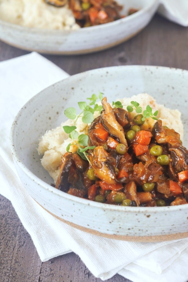 bowl of mushroom stew served over mashed cauliflower, sprig of fresh green thyme on top