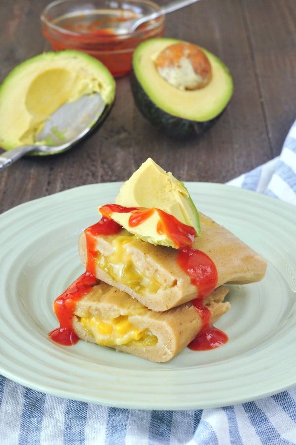 a green chile cheese tamale sliced in half, avocado slices and spicy red sauce on top