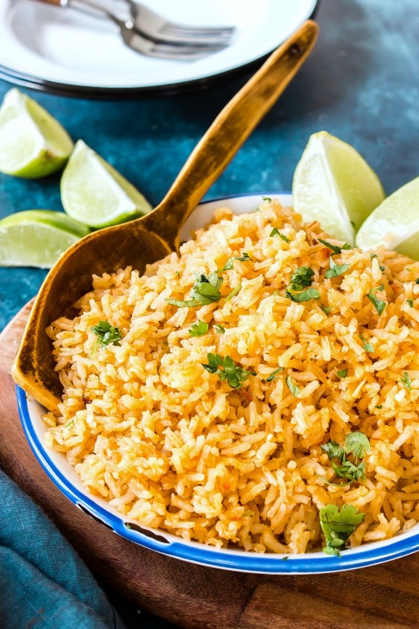 serving bowl of Spanish Rice with lime wedges and wooden spoon, garnished with cilantro
