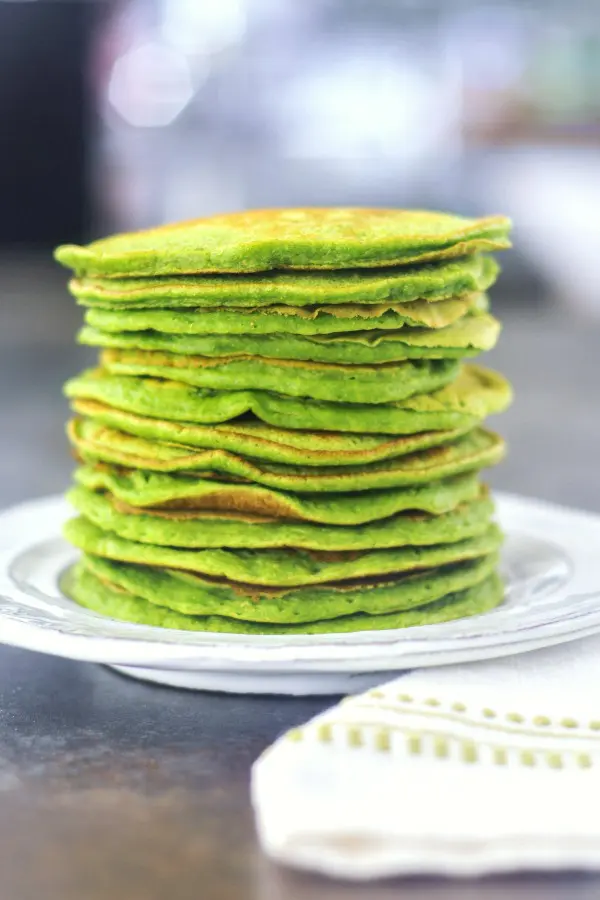 a stack of green pancakes on a white rustic plate.