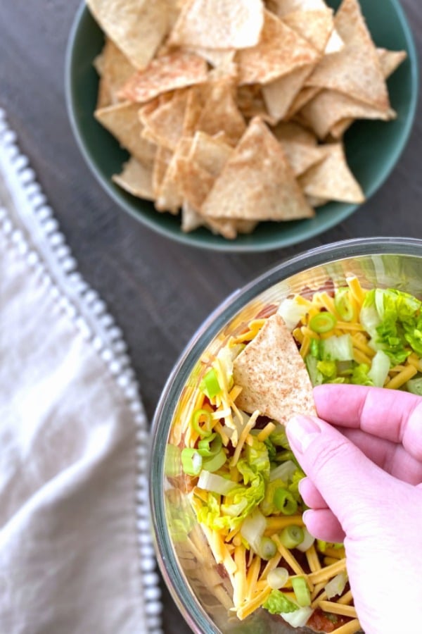 a hand scooping up seven layer dip with a tortilla chip