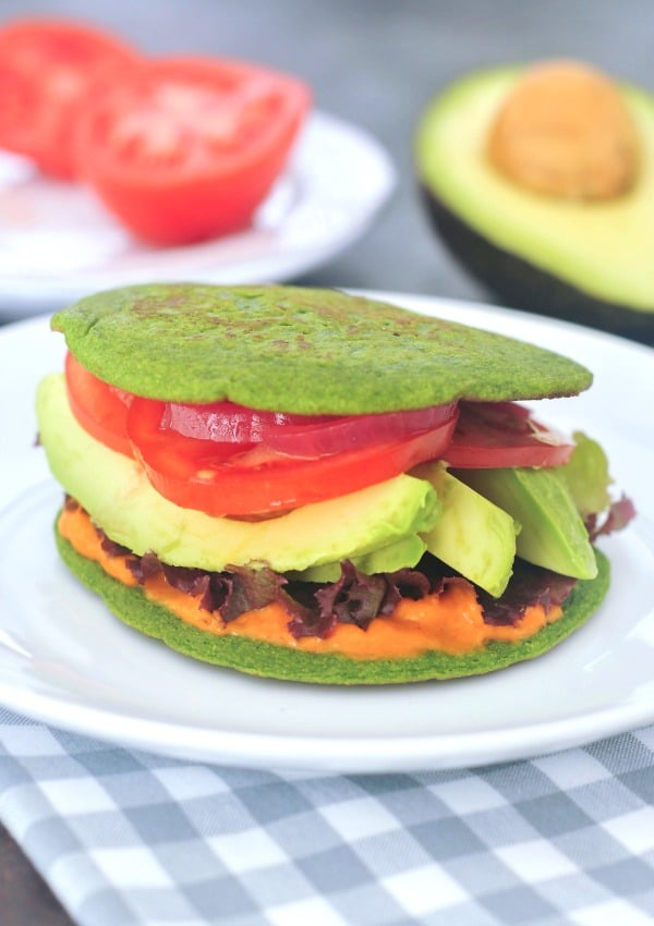 a vegetable sandwich made with spinach pancake bread: hummus, lettuce, sliced avocado, tomato, and onion between bright green pancake 'bread'
