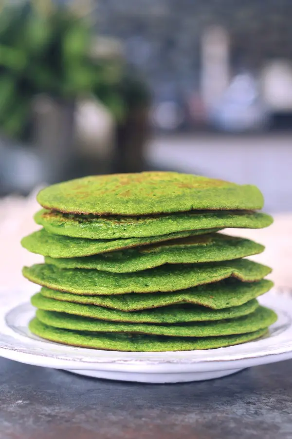 a stack of green spinach pancakes on a white rustic plate.