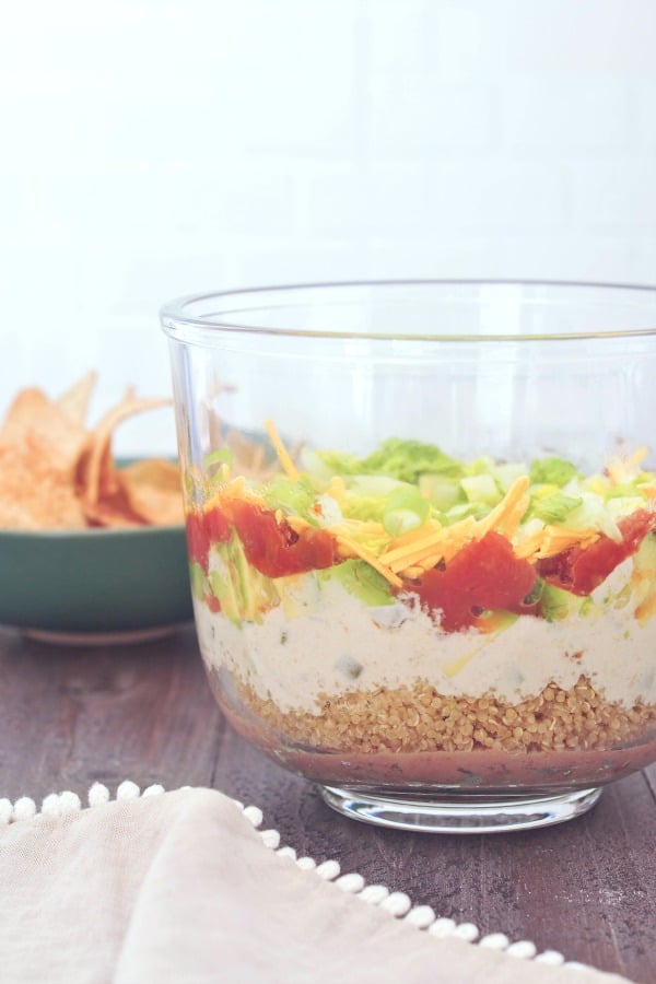 side view of all the layers in seven layer dip: beans, quinoa, cashew cheese sauce, avocado, tomato, green onions and lettuce