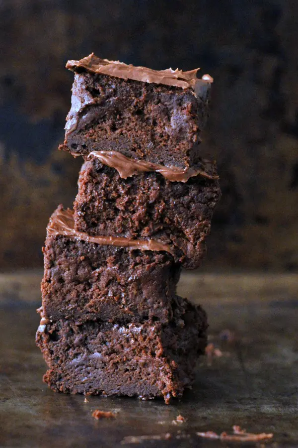 a stack of four frosted vegan brownies against a dark marbled background