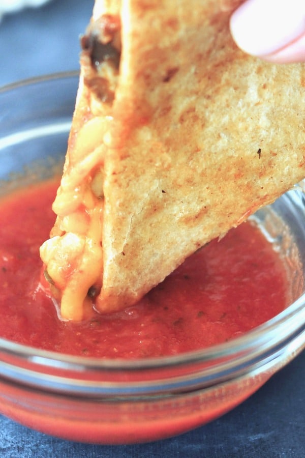 one triangle of a gluten free quesadilla dipped into small glass bowl of pizza sauce