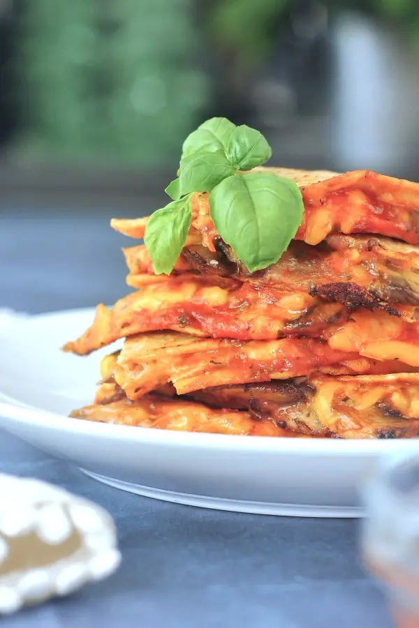 a stack of pizza flavored quesadilla slices on a white plate, fresh basil leaves on top