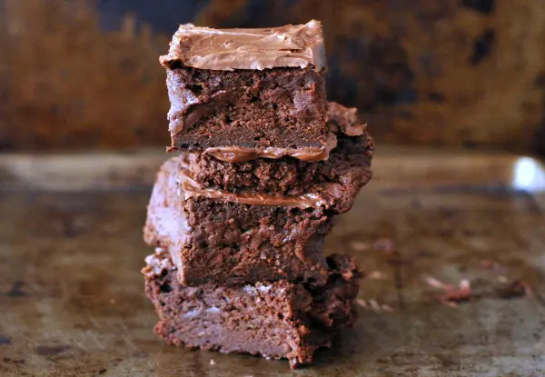 a stack of four frosted vegan brownies against a dark marbled background