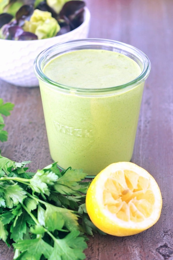 a jar of Green Goddess dressing with a squeezed lemon and a bunch of herbs on the side.