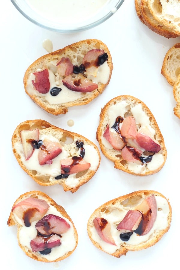 overhead view of sweet cream peach crostini drizzled with balsamic vinegar, on a white platter
