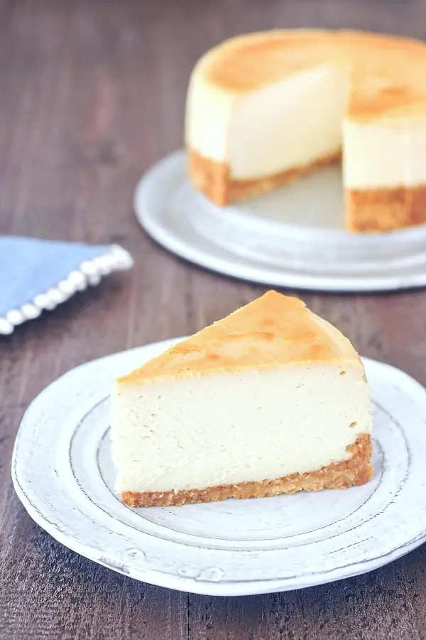 one slice of plain vegan cheesecake on a plate, before adding toppings, full cheesecake in background