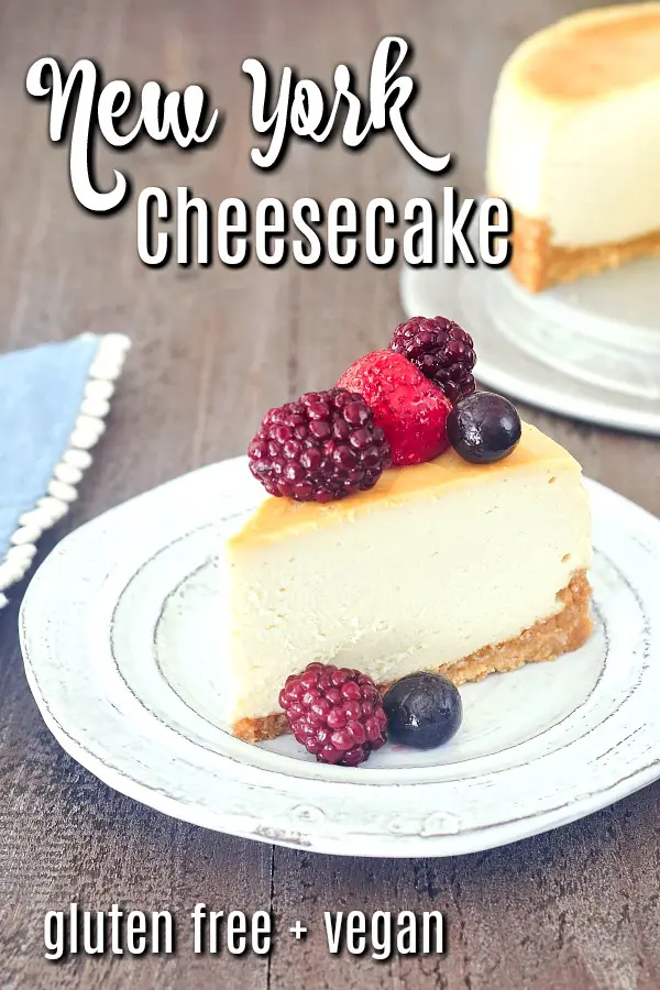 one slice of vegan New York cheesecake on a plate with mixed berries on top, the remaining cheesecake in background