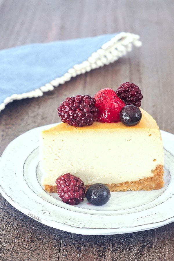 one slice of vegan cheesecake on a rustic white plate with fresh blackberries, blueberries and a strawberry