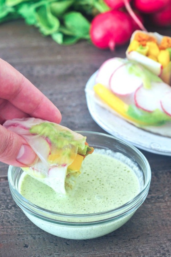 a small glass bowl of light green Dill Ranch Dressing, with a colorful veggie filled salad roll being dipped into it.