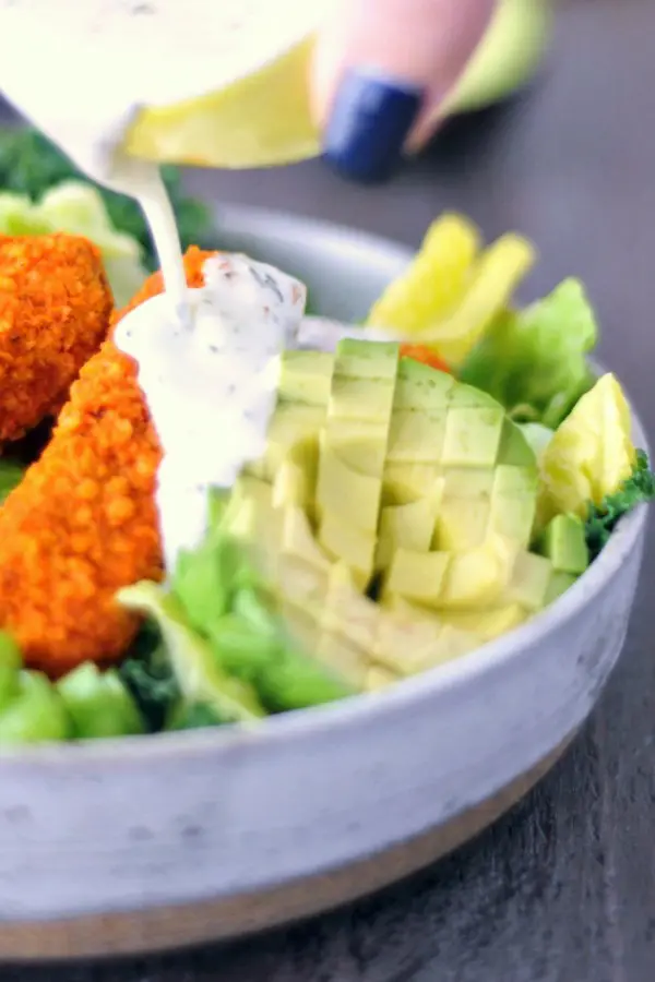 ranch dressing poured over a salad with greens, diced avocado, celery, and buffalo wings