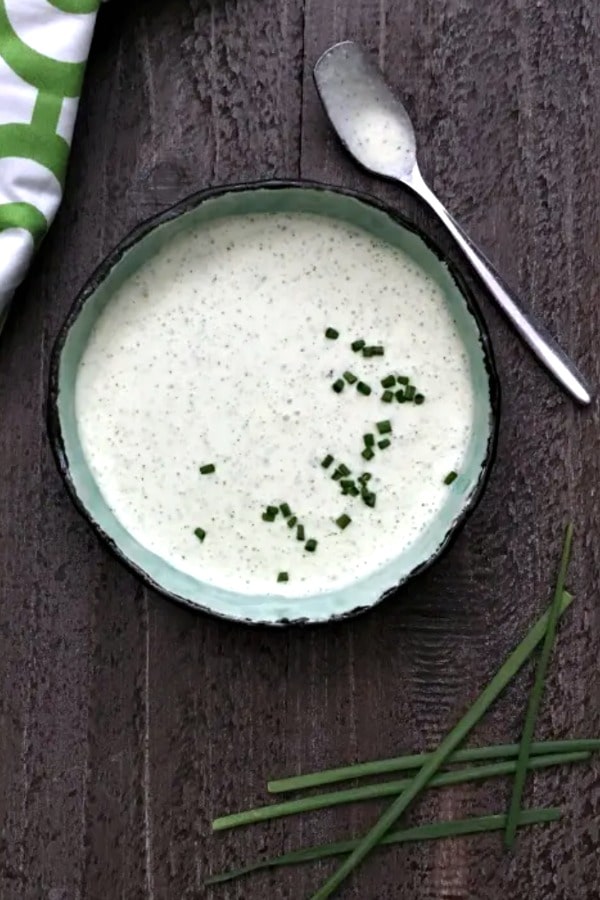 overhead view of vegan ranch dressing in a bowl, topped with chopped chives. green and white napkin and small spoon next to bowl.