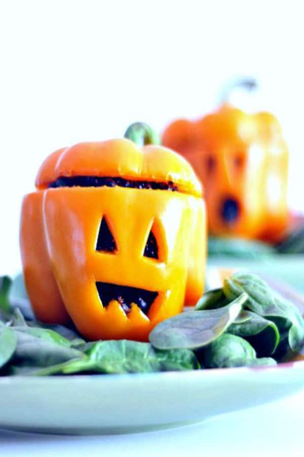 orange bell peppers carved to look like Halloween jack o lanterns, stuffed with black beans and black quinoa, served on a plate over fresh spinach salad