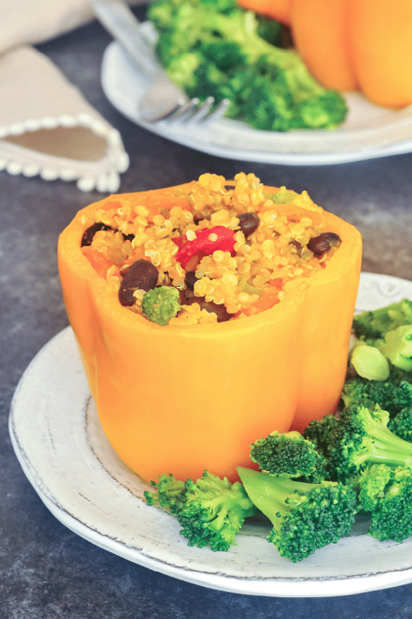 Orange bell peppers stuffed with ginger carrot quinoa, black beans, and broccoli, on a white plate with more broccoli on the side 