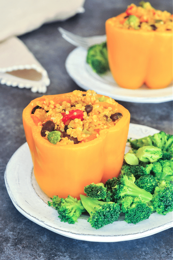 orange bell peppers stuffed with ginger carrot quinoa, black beans, and broccoli, on a white plate with more broccoli on the side 