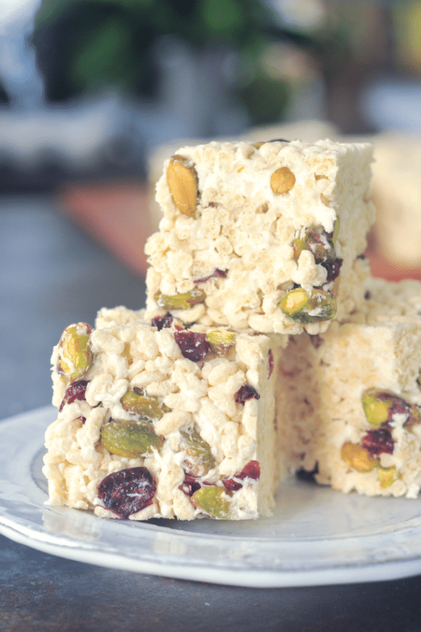 a stack of vegan holiday rice crispies - marshmallow treat squares studded with deep red dried cranberries and bright green pistachios