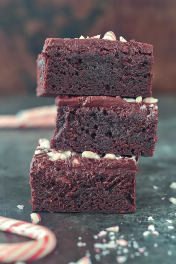 Three brownies in a stack, frosted with vegan chocolate fudge frosting and sprinkled with crushed candy canes.